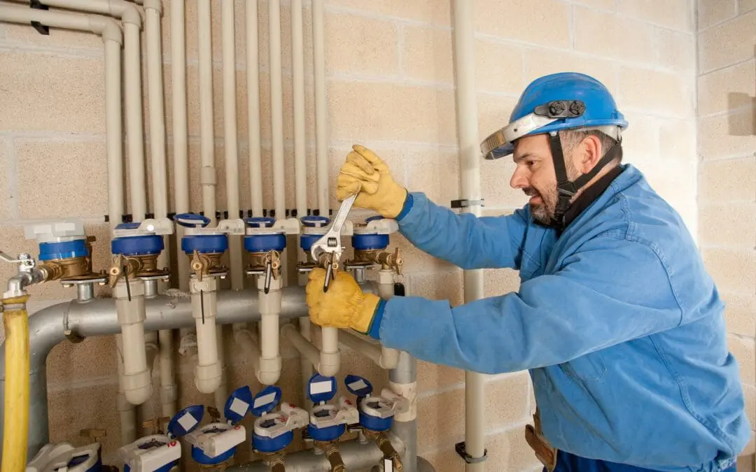 A technician works on plumbing valves in a utility room during the day