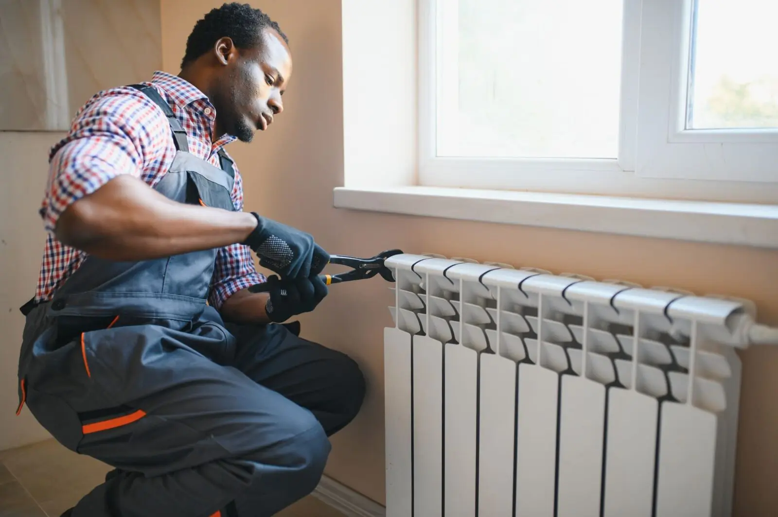afro repairman in overalls using tools while installing or repairing heating radiator afro repairman in overalls using tools while installing or repairing heating radiator
