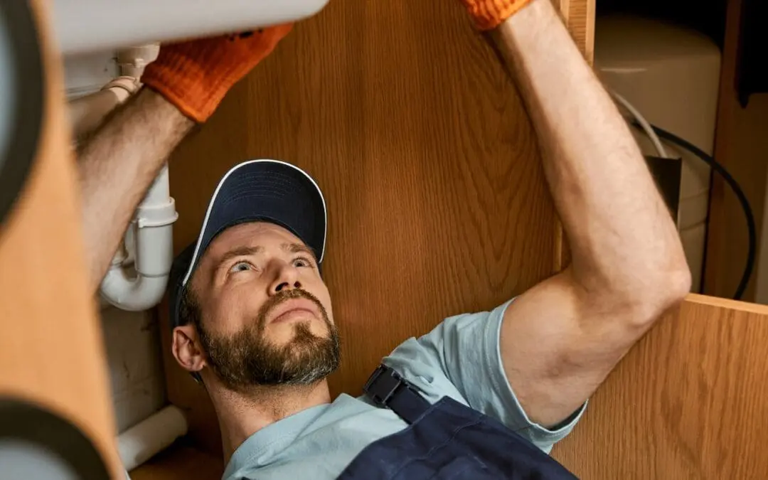 Male plumber fixing sink pipe in kitchen