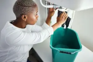 Plumbing, water and a black woman in the bathroom of her home with a cloth and bucket waiting for a