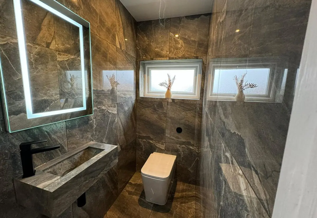 Bathroom fitted by Heat365 in Sheffield with dark marble-effect tiling, a stone basin and an illuminated mirror
